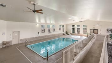 An indoor swimming pool with a ceiling fan, a lifeguard station, and a seating area with a view of the pool.