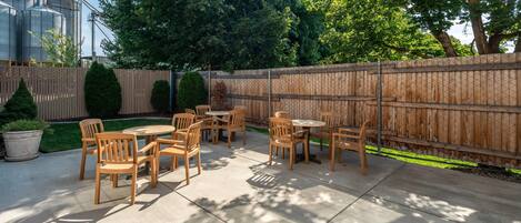 An outdoor patio area with wooden tables and chairs, surrounded by a wooden fence and trees.