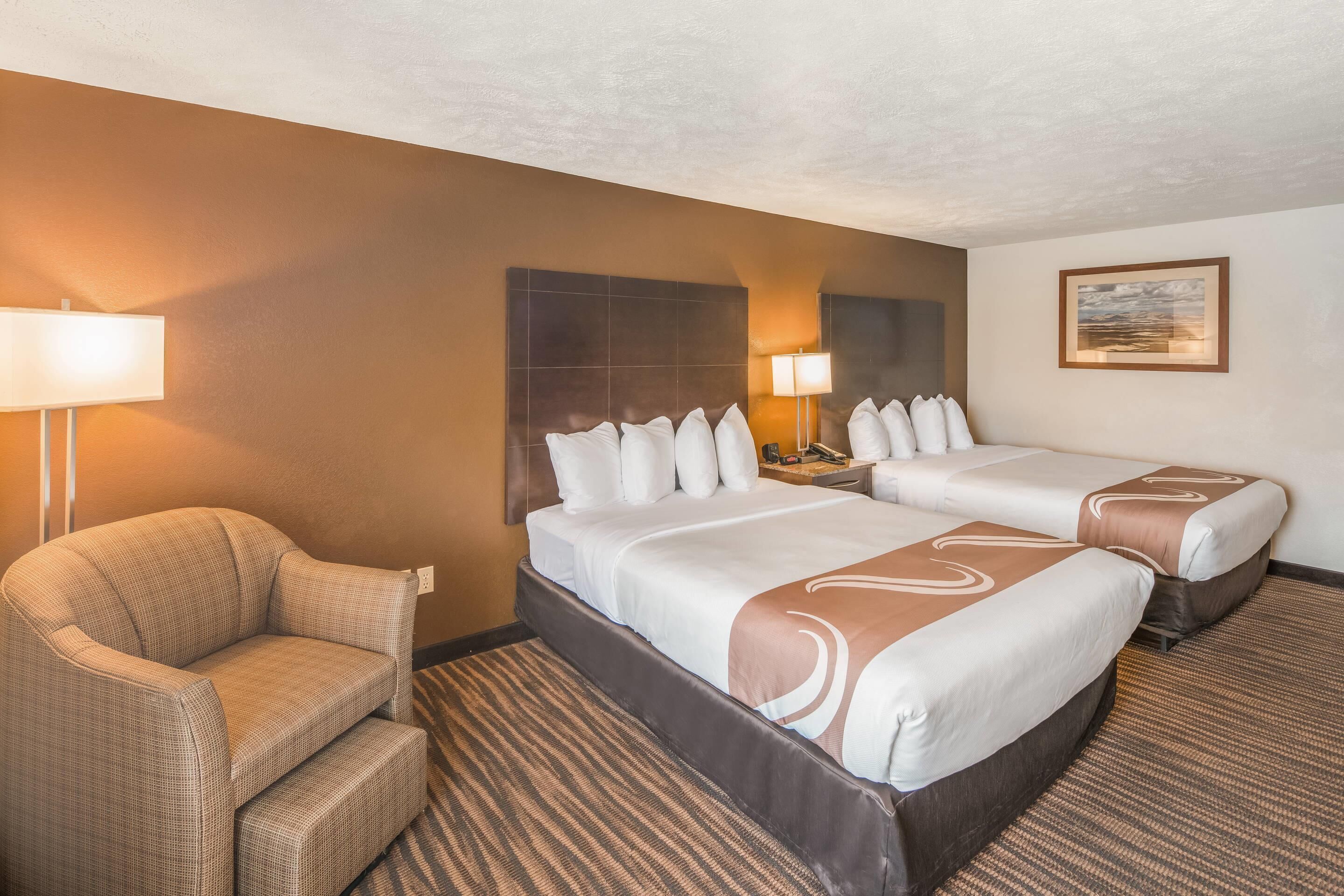 A hotel room with two beds, a sofa, a nightstand, and a lamp.