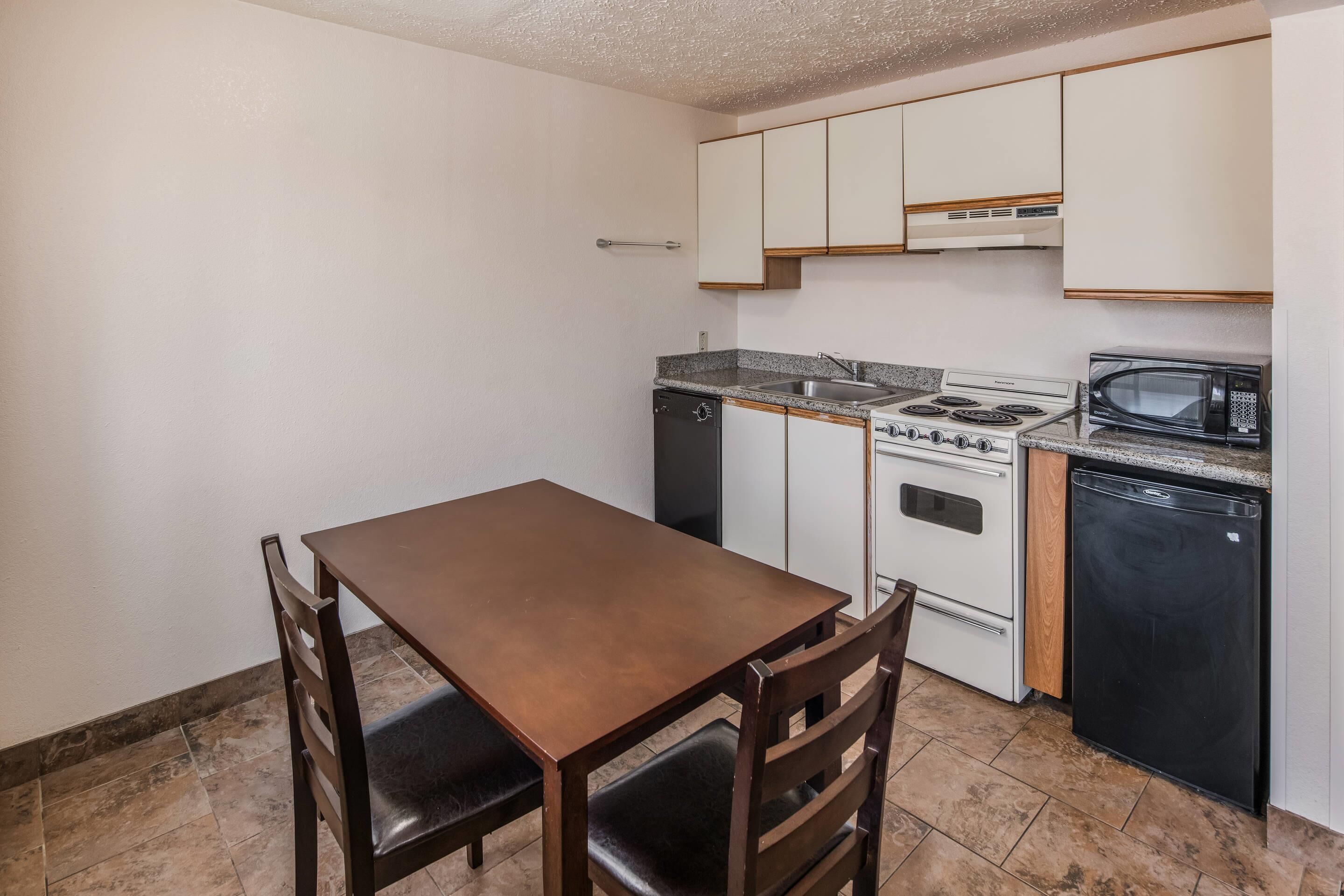 A compact kitchen with a wooden table and chairs, a stove, microwave, and dishwasher.