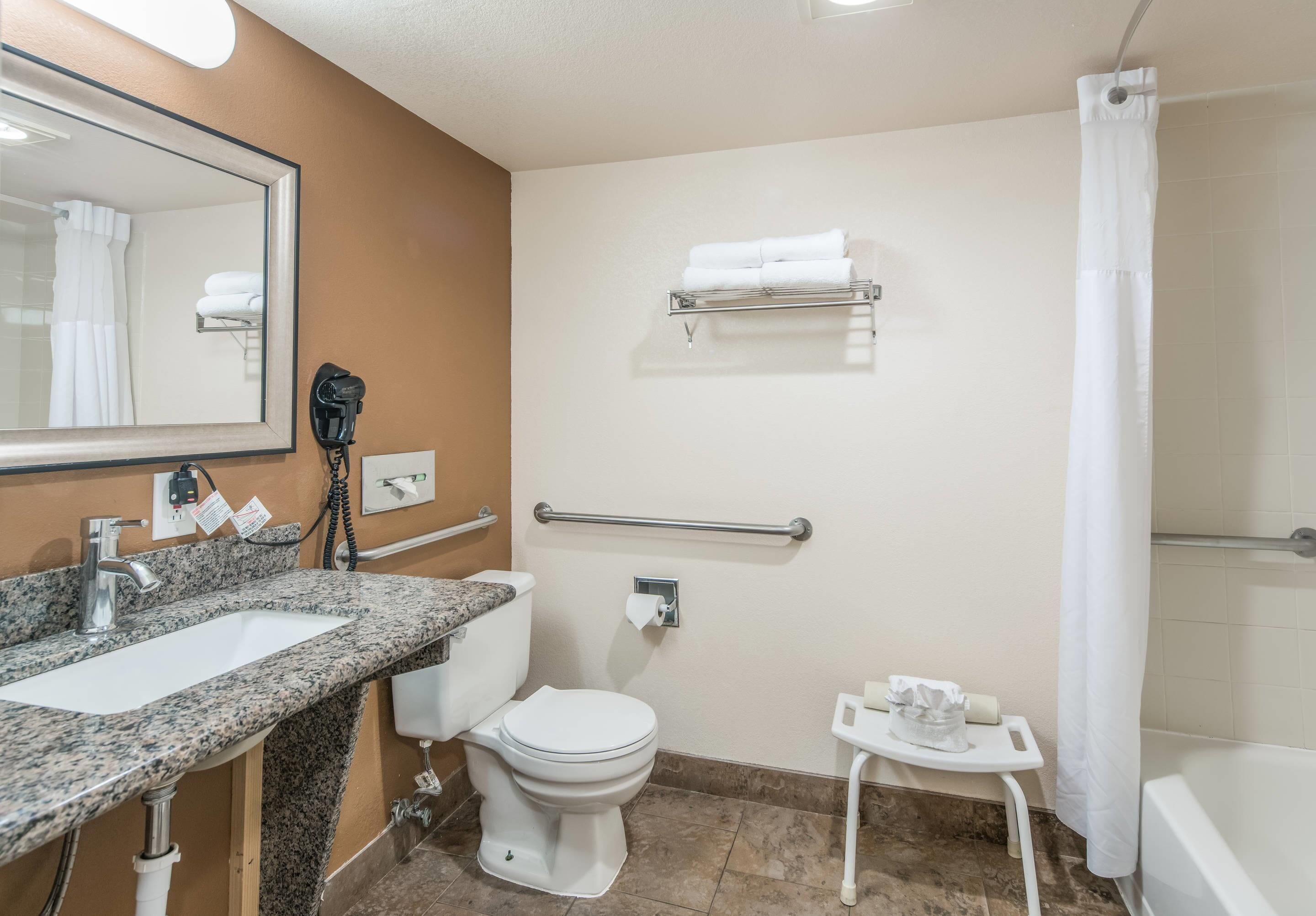 A bathroom with a granite countertop sink, a white toilet, a small white table with toiletries, a towel rack, and a shower curtain.