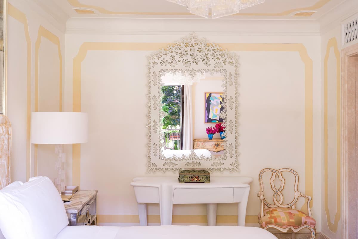 A hotel room with a bed, a desk, a chair, and a mirror.