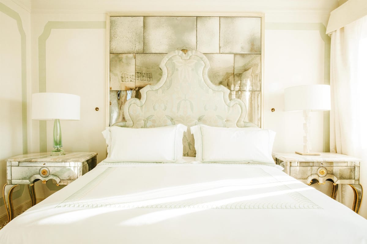 A large bed with a decorative headboard, two bedside tables with lamps, and a mirror on one table.