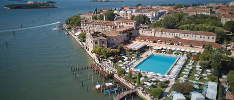 An aerial view of a coastal hotel with a swimming pool, multiple buildings, and a marina.