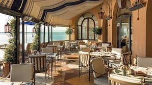 Un restaurant doté d’une terrasse offrant une vue sur un plan d’eau, avec un plafond décoré de motifs et un décor classique.