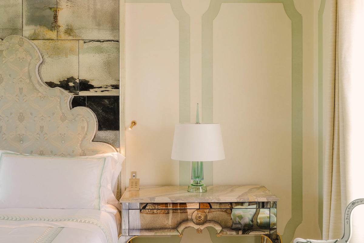 A hotel room with a bed, a nightstand with a lamp, and a wall with a geometric pattern.