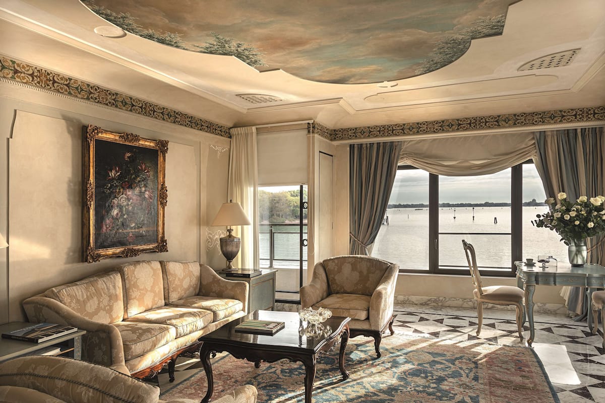 A luxurious room with a sofa, armchair, and a view of a body of water through large windows.