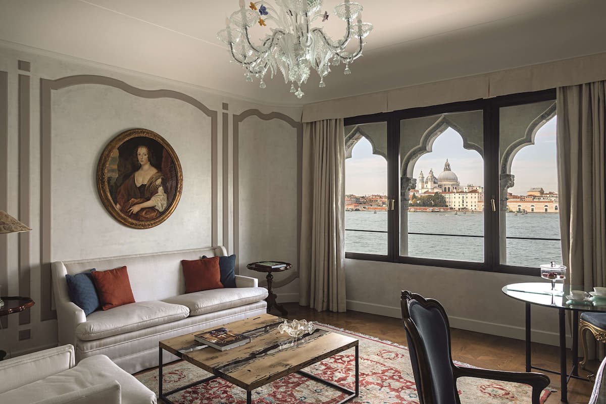 A room with a white sofa, a coffee table, and a view of a historic building across a body of water.