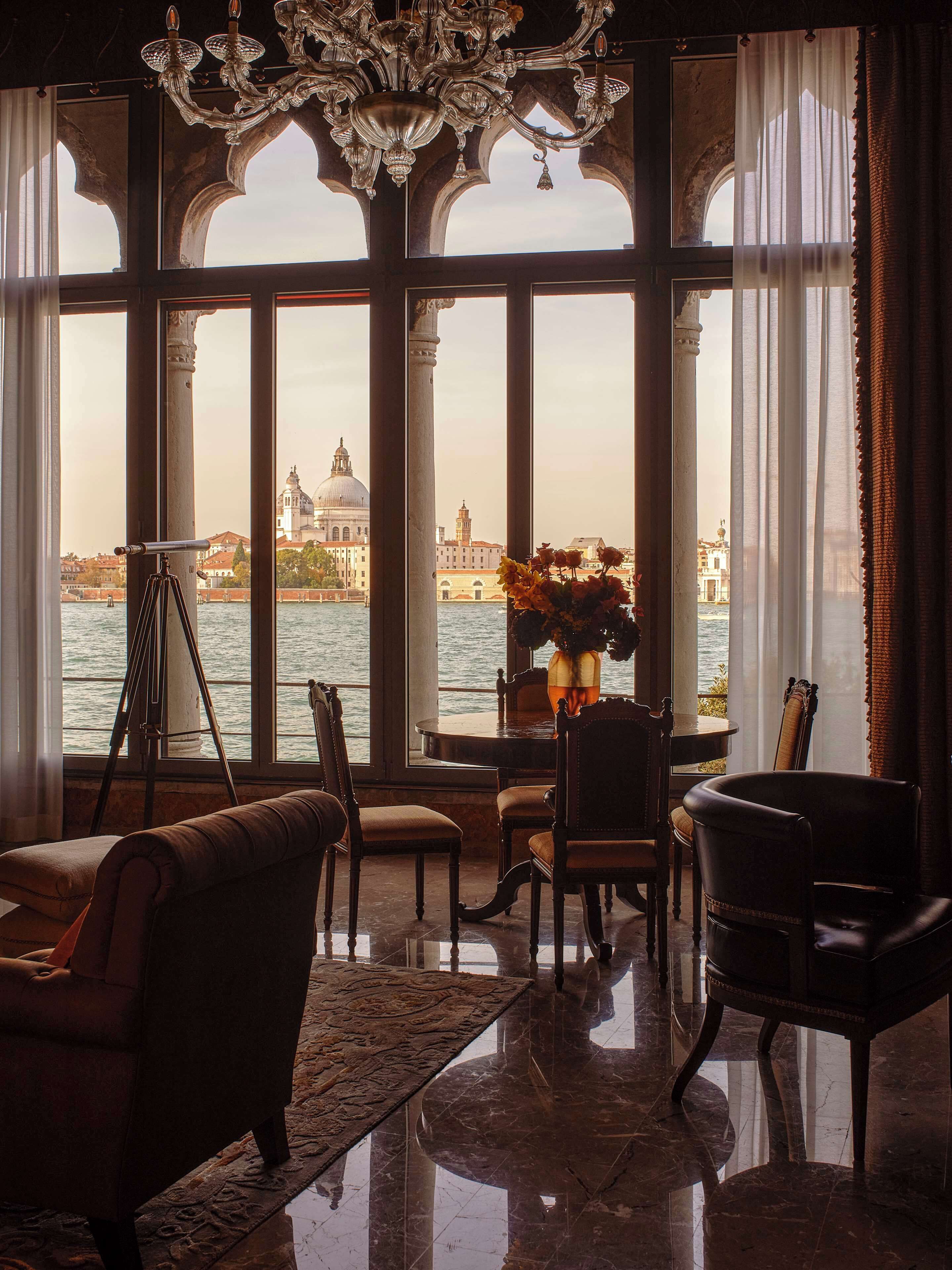 Une chambre avec vue sur Venise, comprenant un lustre, un trépied et une table avec des chaises.