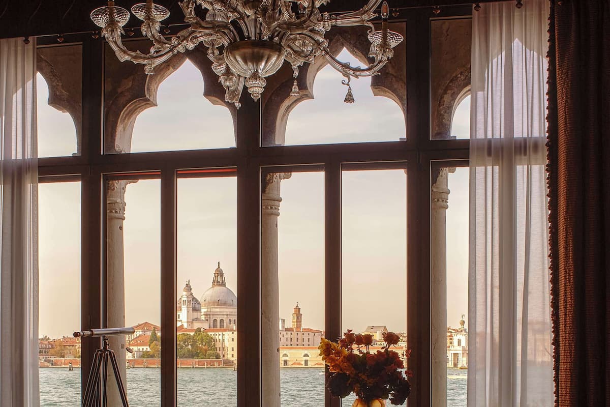 A room with a view of Venice, featuring a chandelier, a tripod, and a table with chairs.