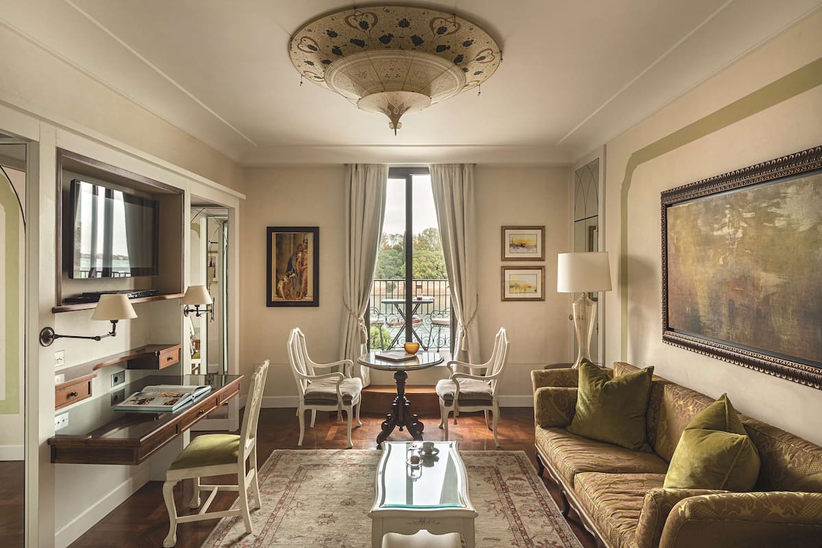 A room with a dining table, two chairs, a sofa, a TV, and a large painting on the wall.
