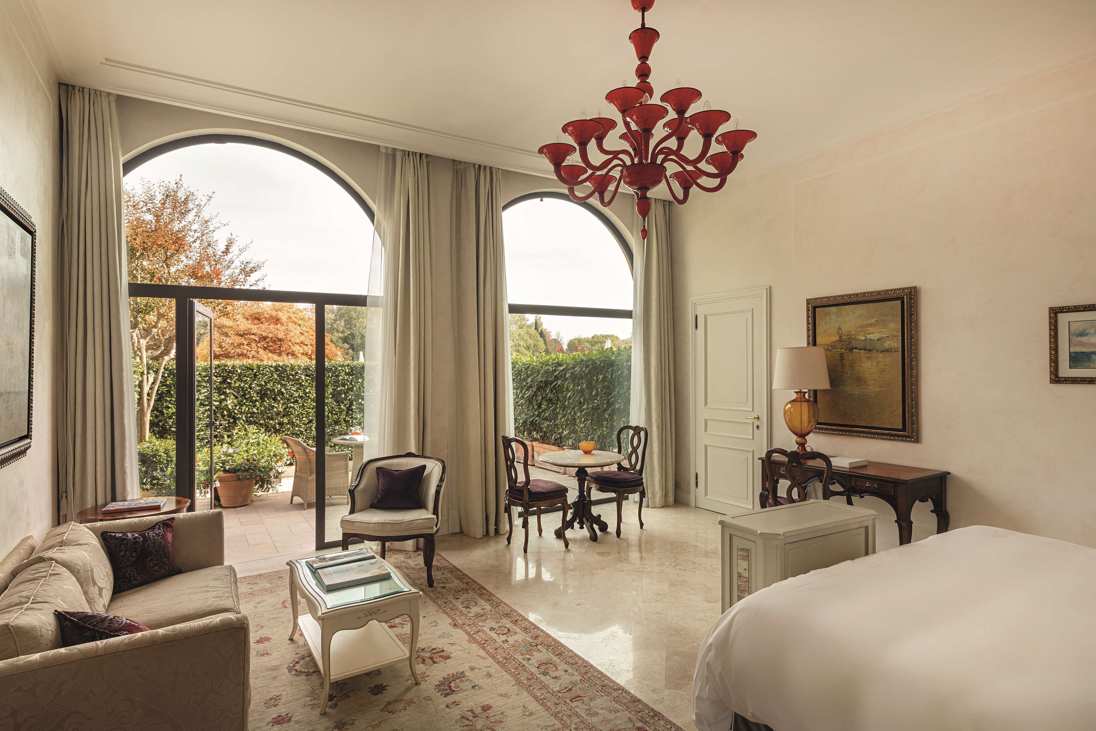 Une chambre d’hôtel avec un grand lit, un canapé, une table à manger avec des chaises et un lustre.