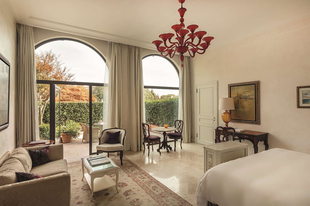 A hotel room with a large bed, a sofa, a dining table with chairs, and a chandelier.
