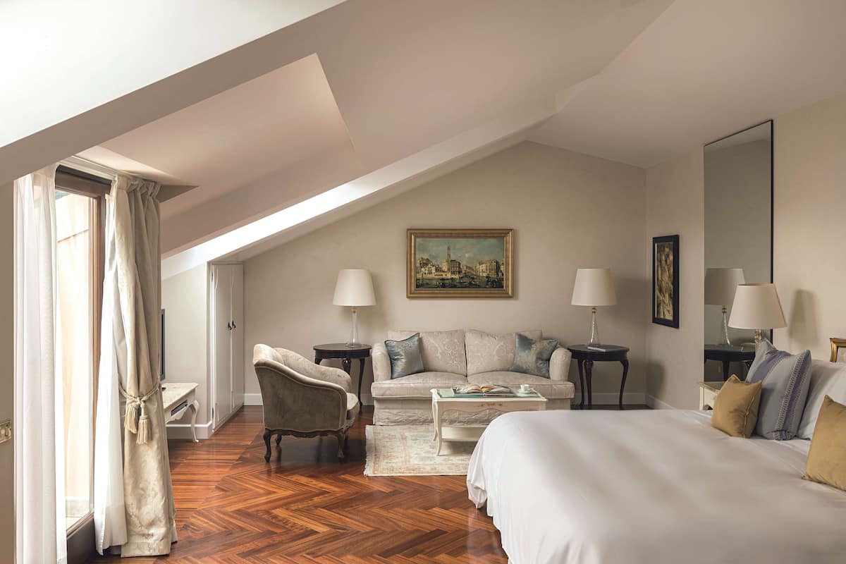 A hotel room with a bed, a sofa, a chair, a desk, and a painting on the wall.