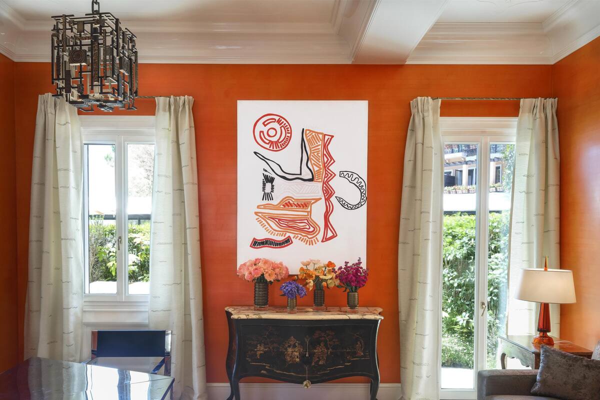 A room with a large abstract painting, a glass coffee table, a sofa, and a console table with vases.