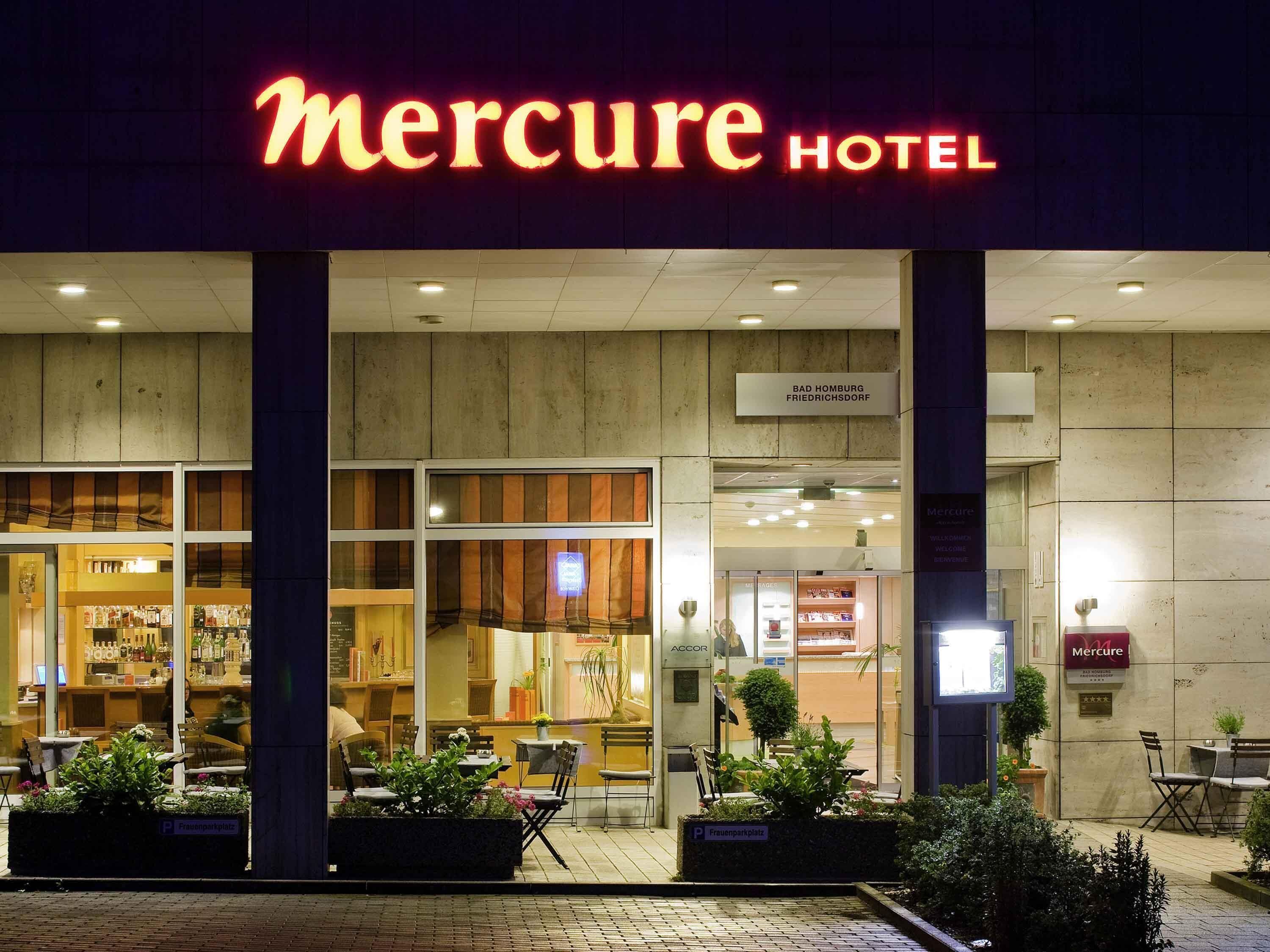 El exterior del Hotel Mercure, con un letrero visible, un bar a través de la ventana y un área de estar al aire libre.