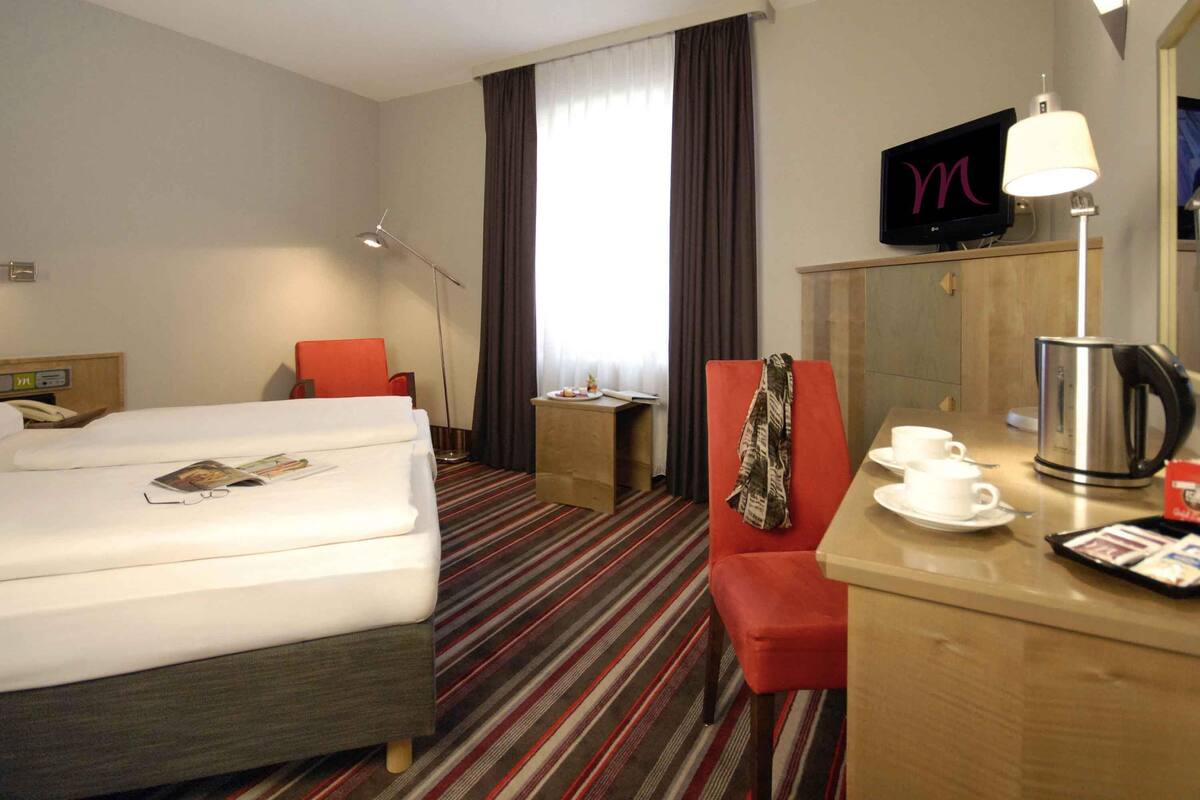 A hotel room with a bed, a desk, a chair, a television, and a coffee maker.