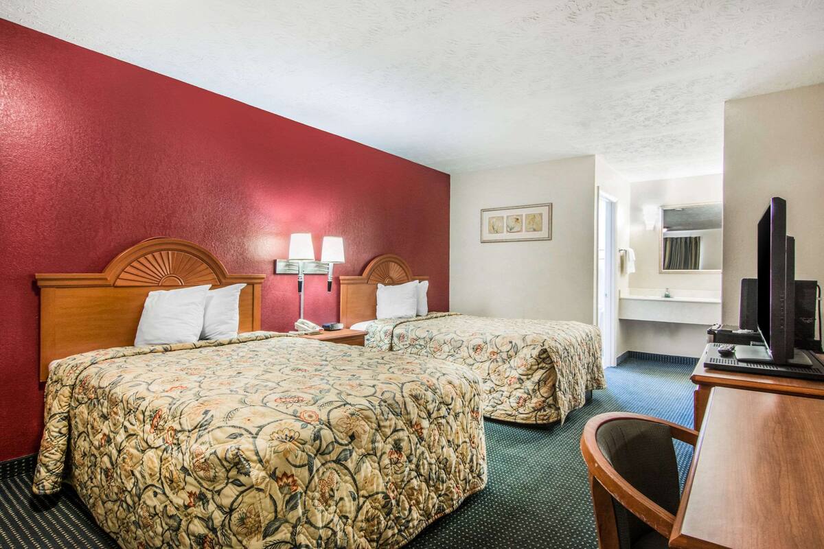 A hotel room with two beds, a desk, a TV, and a window.