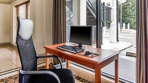 A room with a wooden desk, a black chair, a computer setup, and a view of a staircase and outdoor area. - Rodeway Inn La Grange East (LaGrange)