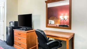 A hotel room with a wooden desk, a black chair, a TV, a small refrigerator, and a dresser with drawers. - Rodeway Inn La Grange East (LaGrange)