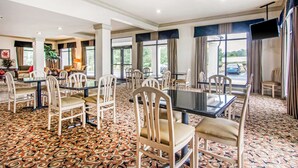 A spacious dining area with multiple tables and chairs, large windows with curtains, and a patterned carpet. - Rodeway Inn La Grange East (LaGrange)