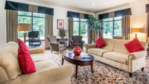 A spacious living room with two beige sofas, a coffee table, and a patterned carpet. - Rodeway Inn La Grange East (LaGrange)
