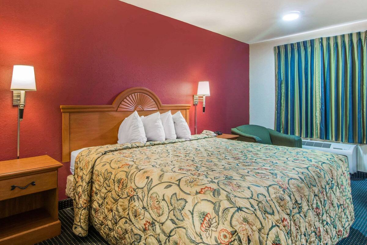 A hotel room with a large bed, two bedside lamps, a headboard, and a window with curtains.