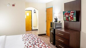 Habitación de hotel con cama, televisión, refrigerador, microondas y armario de madera.