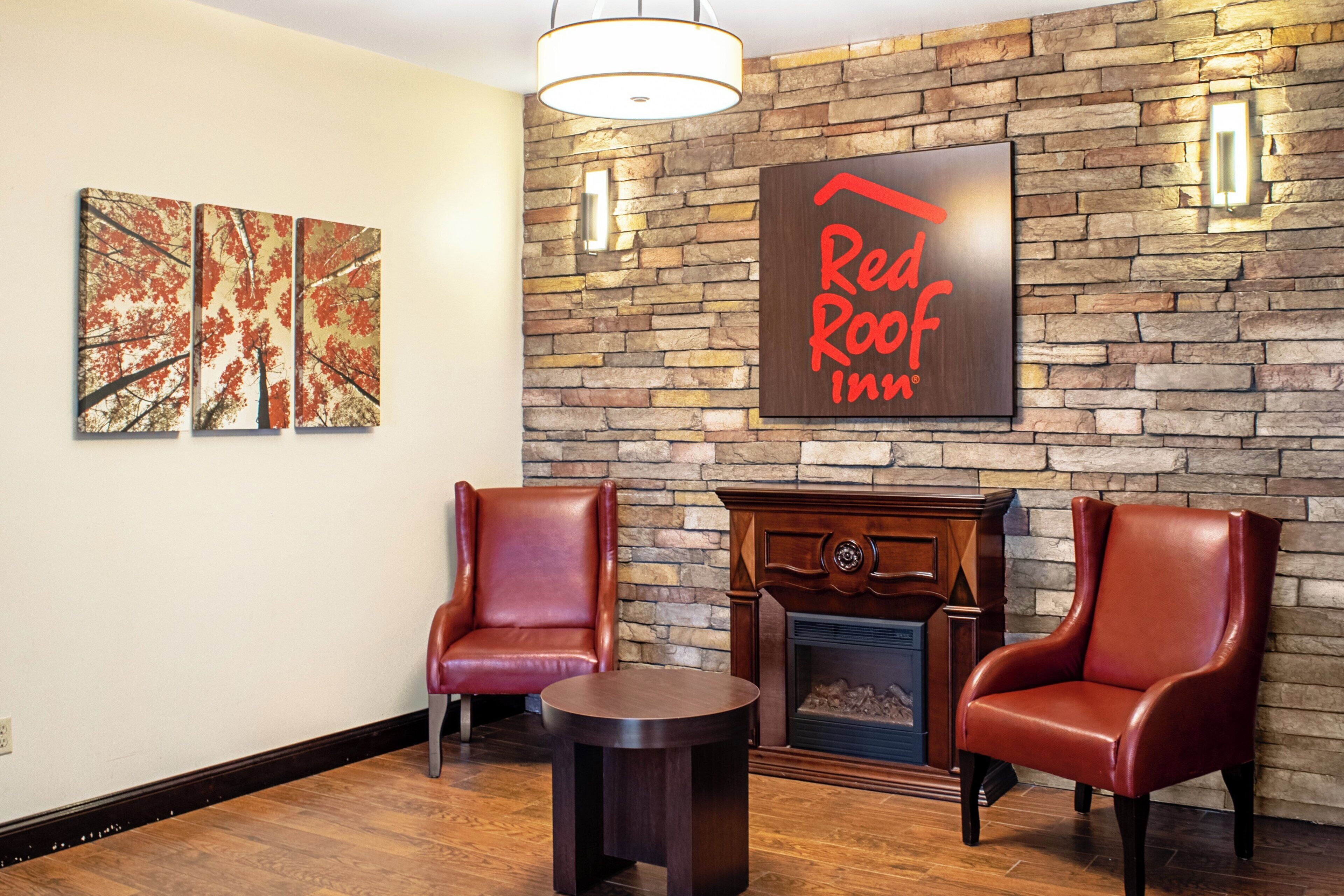 El vestíbulo de un Red Roof Inn con una pared de piedra, dos sillones de cuero, una mesita redonda y una chimenea.