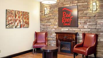 El vestíbulo de un Red Roof Inn con una pared de piedra, dos sillones de cuero, una mesita redonda y una chimenea.