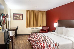A hotel room with a bed, a desk, a chair, an air conditioner, and a TV.