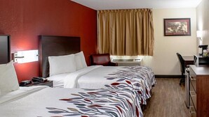Habitación de hotel con dos camas, un escritorio, una silla, un equipo de aire acondicionado y un cuadro en la pared.