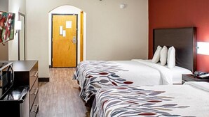 Una habitación de hotel con dos camas, un escritorio, un televisor y una puerta.