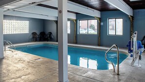 Ein Hallenbad mit klarem Wasser, umgeben von Wänden mit Fenstern und einer Decke mit freiliegenden Rohren.