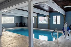 Una piscina interna con acqua cristallina, circondata da pareti dotate di finestre e un soffitto con tubature a vista.