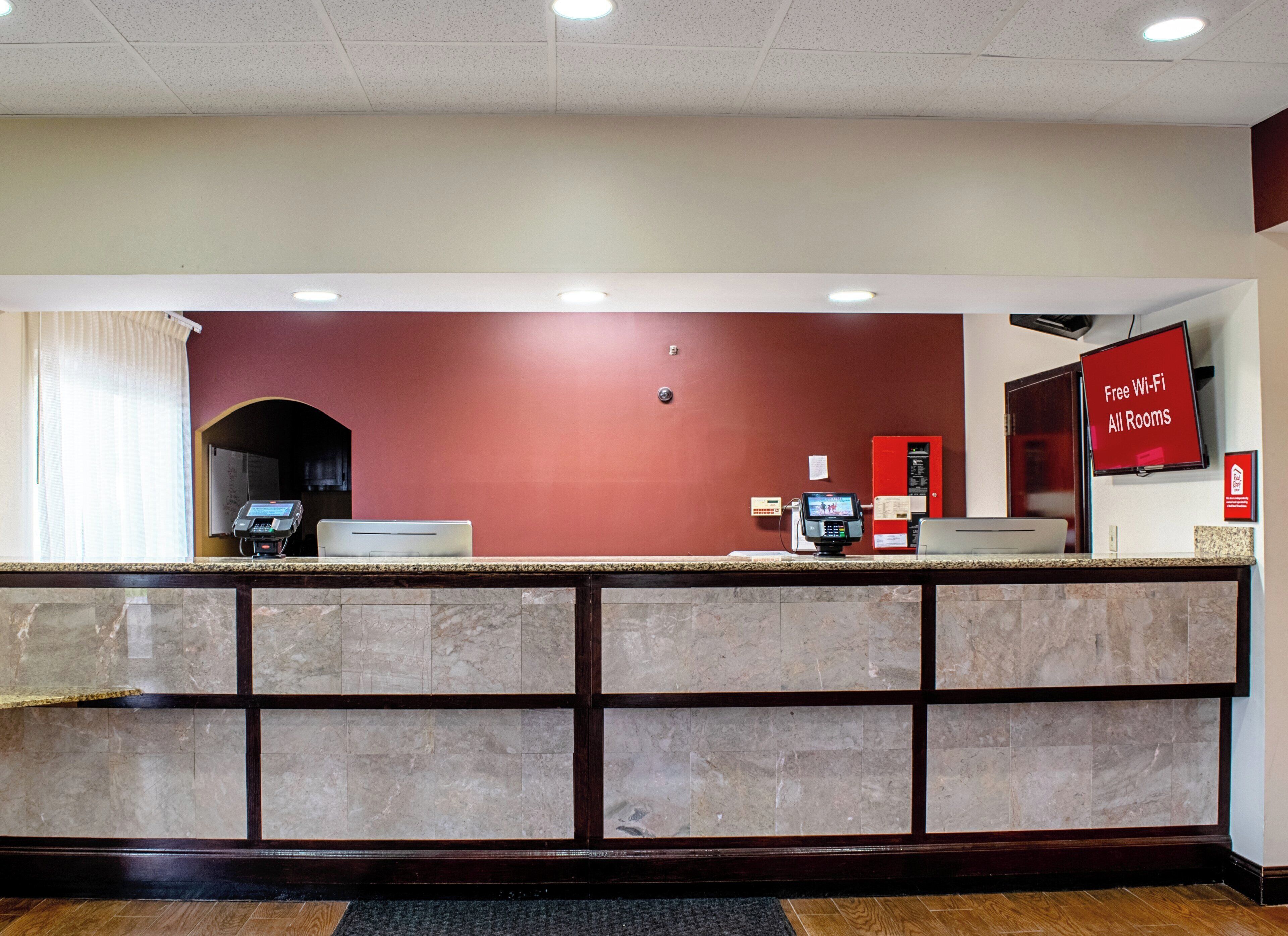 Zona de recepción de hotel con mostrador de mármol, pared roja e indicación de Wi-Fi gratuito.