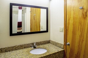 A bathroom with a granite countertop, a sink, a mirror, and a wooden door.
