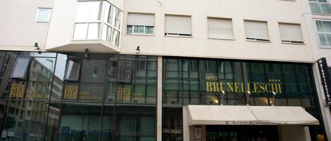 Un hotel moderno con amplios ventanales de vidrio, alfombra roja en la entrada y un cartel que dice "Hotel Bruneleschi".