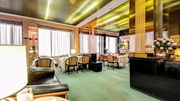 A hotel lobby with a green carpet, leather seating, and a dining area with tables and chairs.