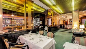 A restaurant with tables set for dining, a bar area with bottles, and a green carpeted floor. - Hotel Brunelleschi (Milan)