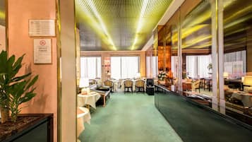A hotel lobby with a green carpet, leather sofas, and a mirrored wall reflecting the interior.