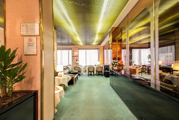 A hotel lobby with a green carpet, leather sofas, and a mirrored wall reflecting the interior.