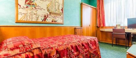 A hotel room with a bed, a desk, a chair, a television, and a large painting on the wall.