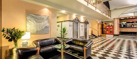 Een hal met leren banken, een glazen tafel, een plant en een geruite vloer.