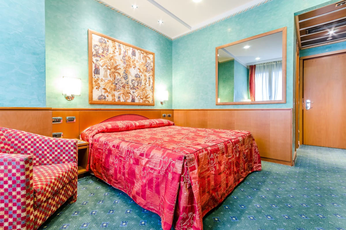 A hotel room with a bed, a sofa, a large painting, a mirror, and a door.