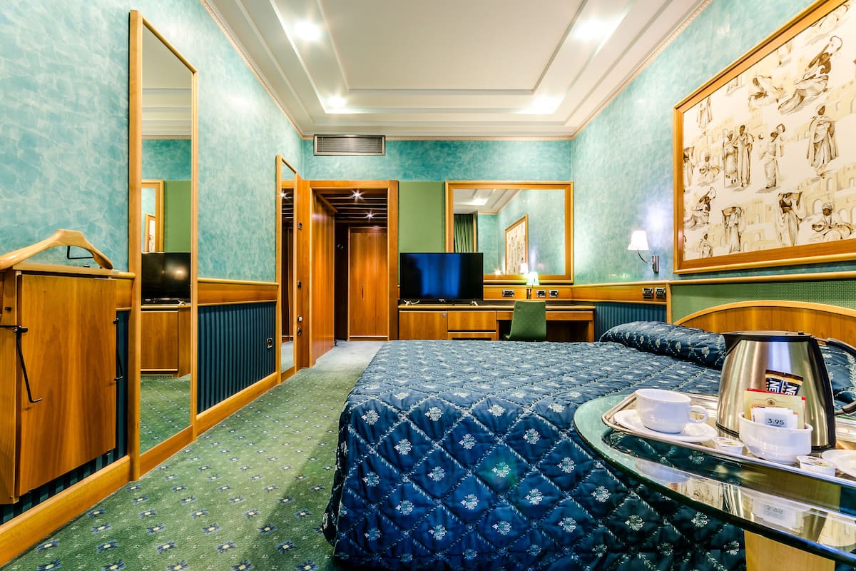 A hotel room with a bed, a desk, a television, and a coffee maker on a tray.