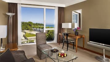 A hotel room with a large window, a sofa, a glass coffee table with snacks, a TV, and a desk with a lamp.