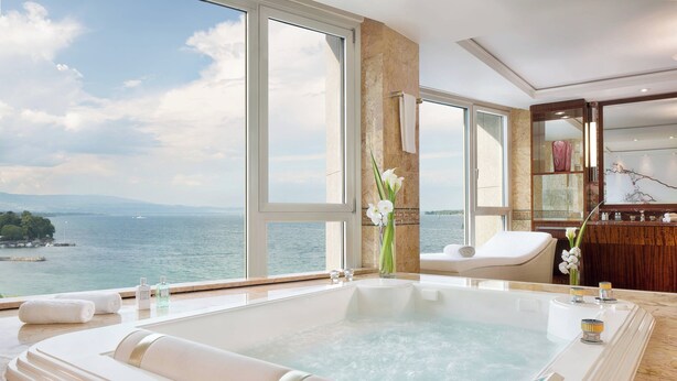 Un baño lujoso con una bañera grande, un espacio de descanso y vista al mar.