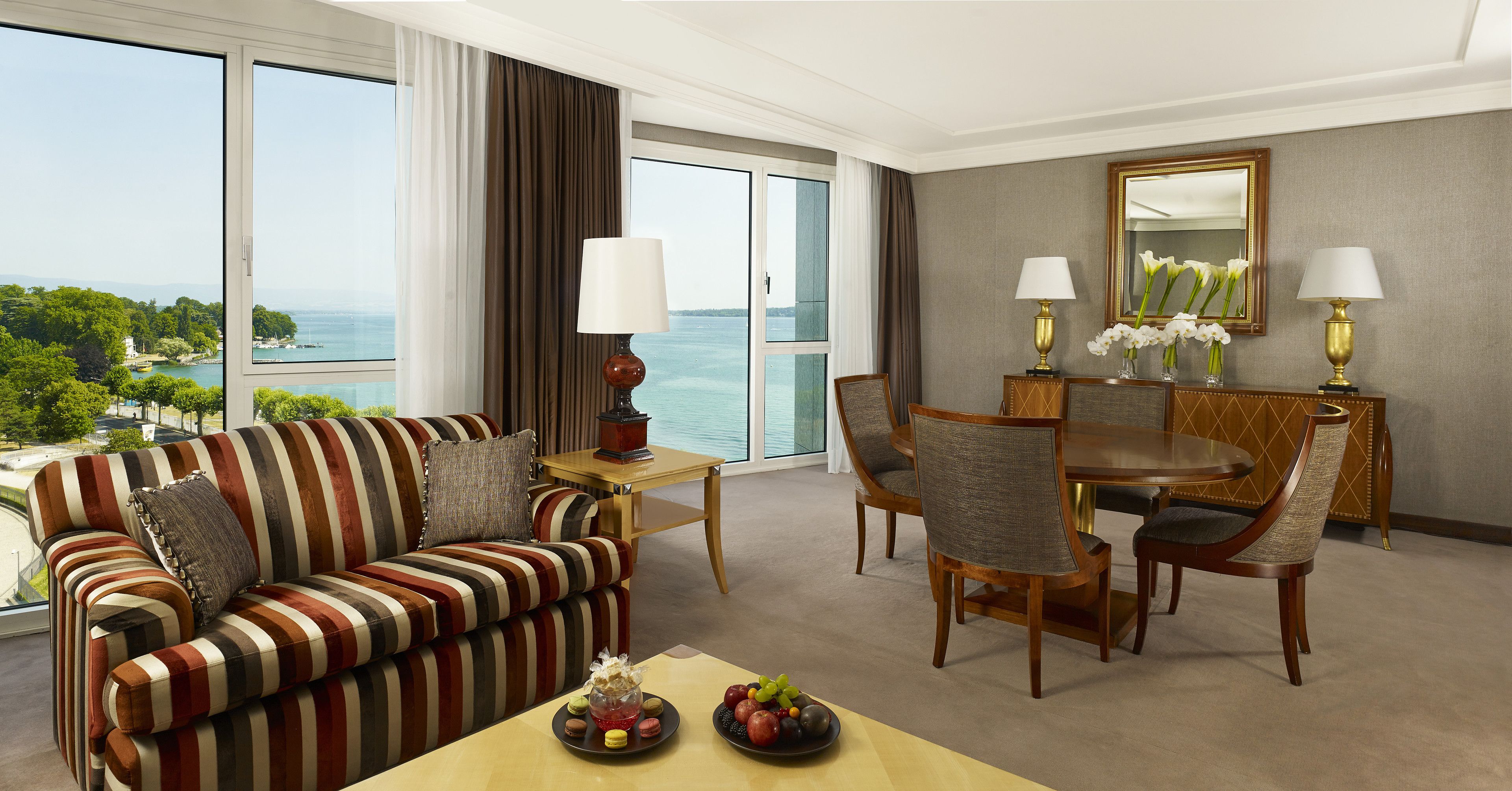 Une chambre d’hôtel avec un canapé à rayures, une table à manger, des chaises et une vue sur la mer.