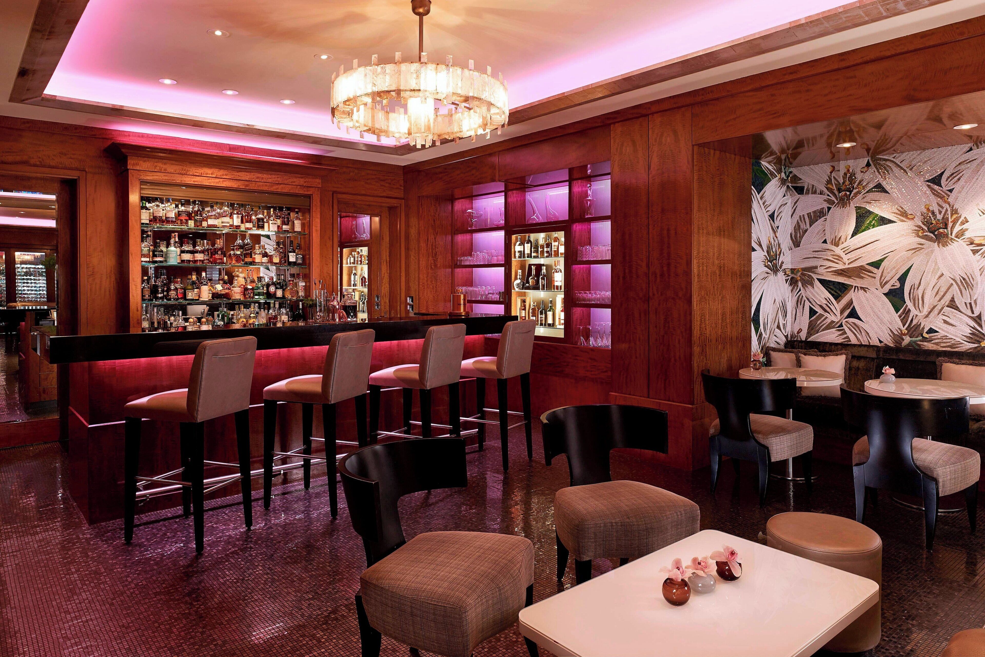 Un área de bar con diversas opciones de asientos, como taburetes y mesas redondas, y una pared decorativa con motivos florales.